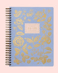 A light blue planner with gold foiled rose detailing, spiral bound and text in the center that reads, "Rifle Paper Co 24-25 17 Month Planner". 