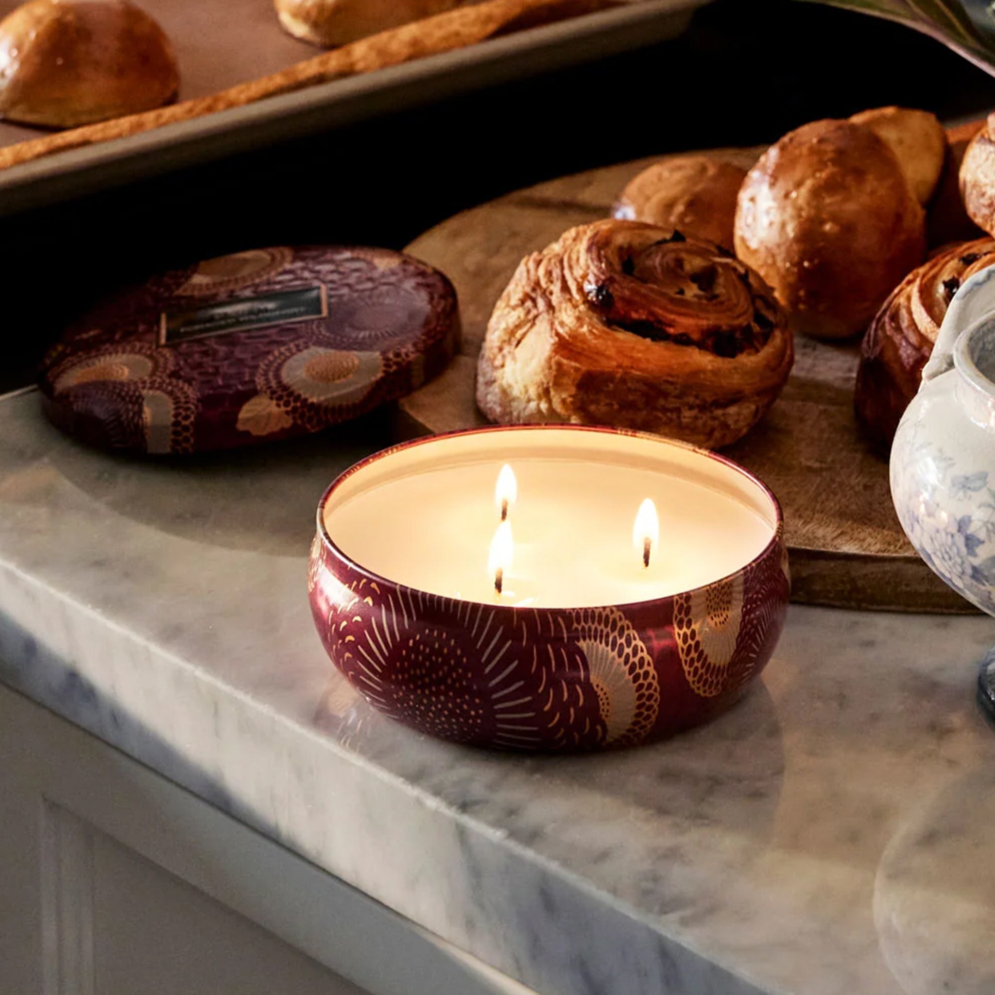 A red and tan floral print metal tin with a three wick candle inside. 