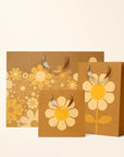 On an ivory background is three brown gift bags with yellow daisies on them. 