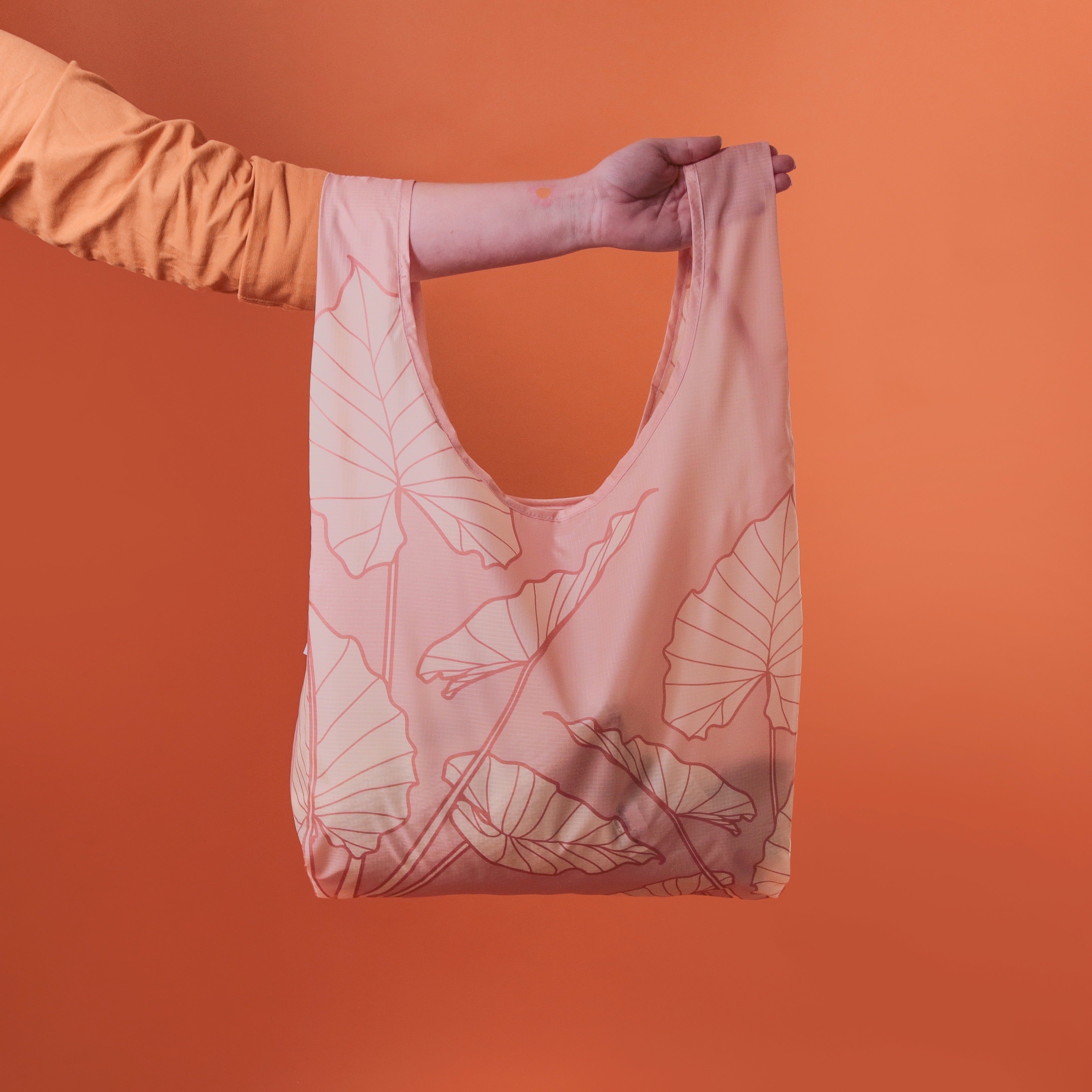 A light pink nylon reusable tote bag with an alocasia leaf print. 