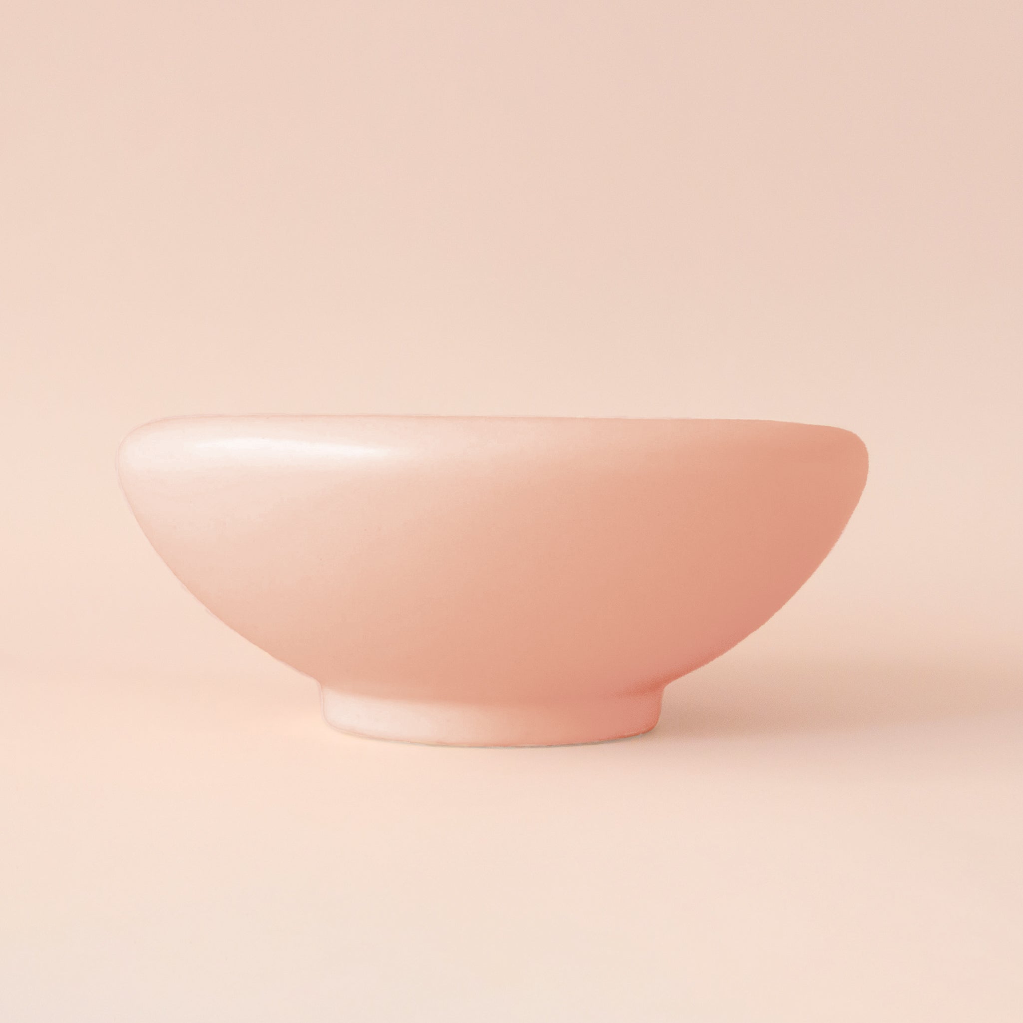 A light pink ceramic low bowl planter with a rounded edge. 