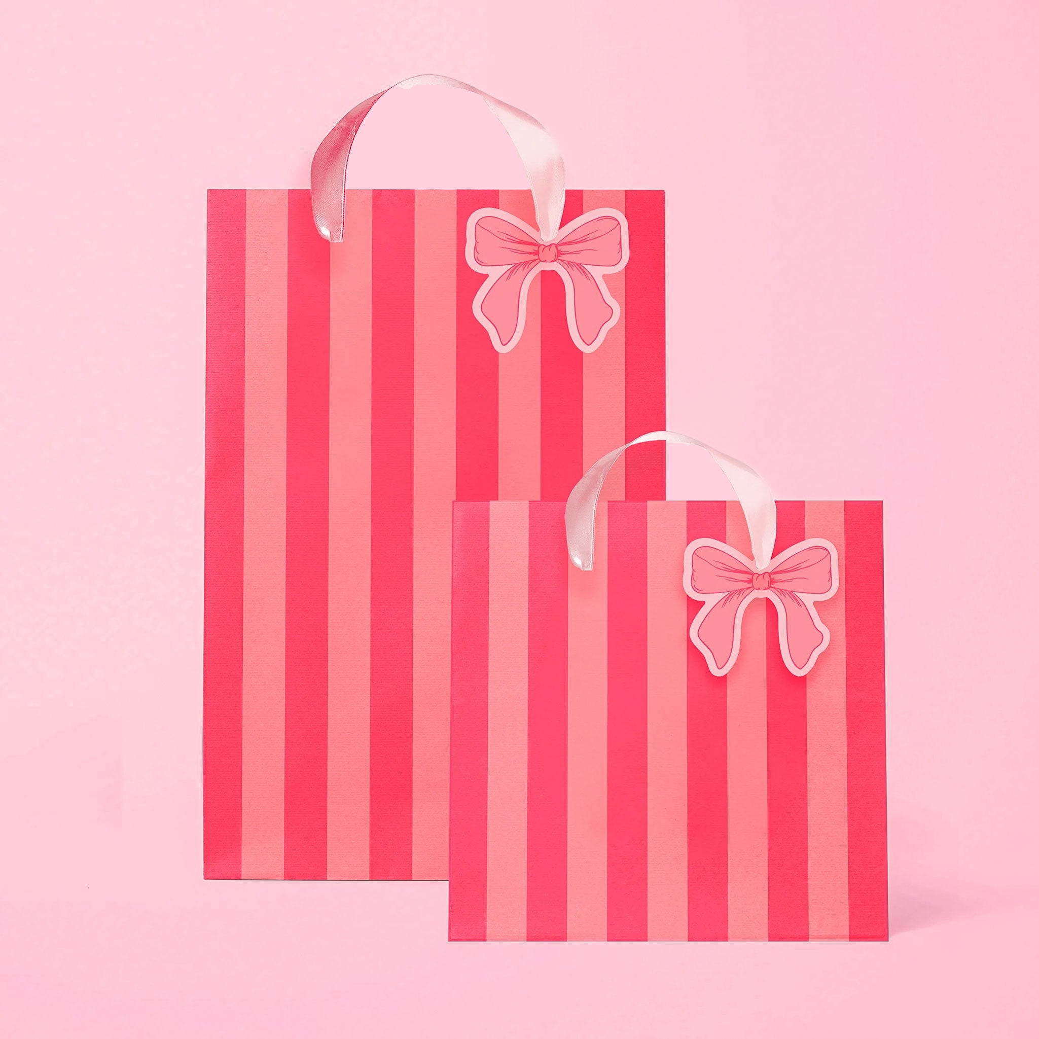 A light pink and hot pink striped gift bag in two different sizes with ribbon handles and a small bow shaped tag.