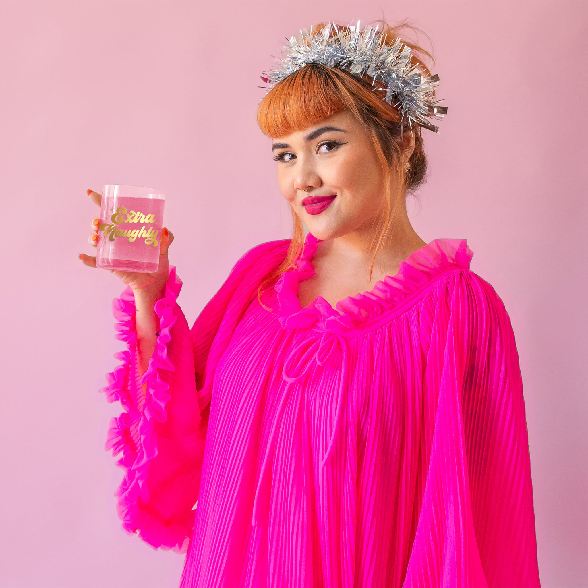 A model holding a glass tumbler with gold text that reads, &#39;Extra Naughty&#39;. 