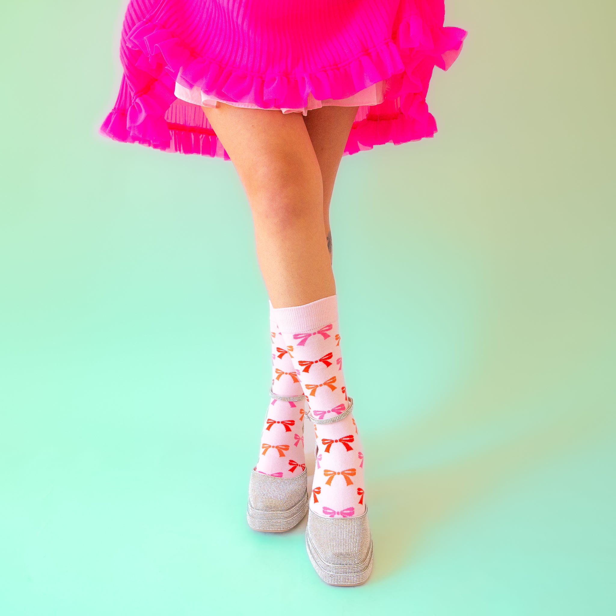 A pair of light pink socks with red, orange and pink bow patterns all over. 