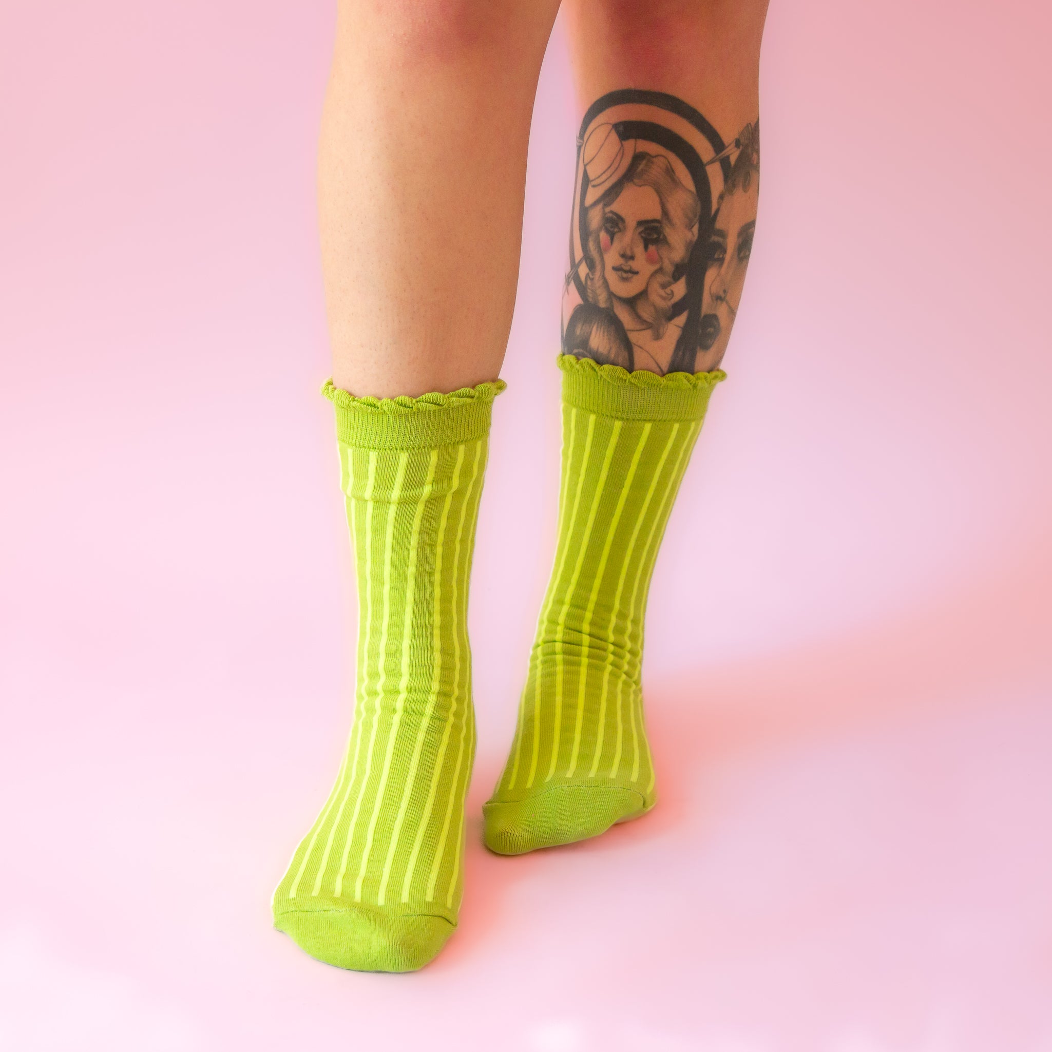 A model wearing a pear of lime green striped socks with a ruffle detail at the top. 