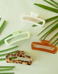 On a mint background is the mist cabana hair claw sitting next to three different color ways of the clip.