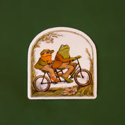 A toad and frog graphic riding on a bicycle on an arched shaped sticker. 