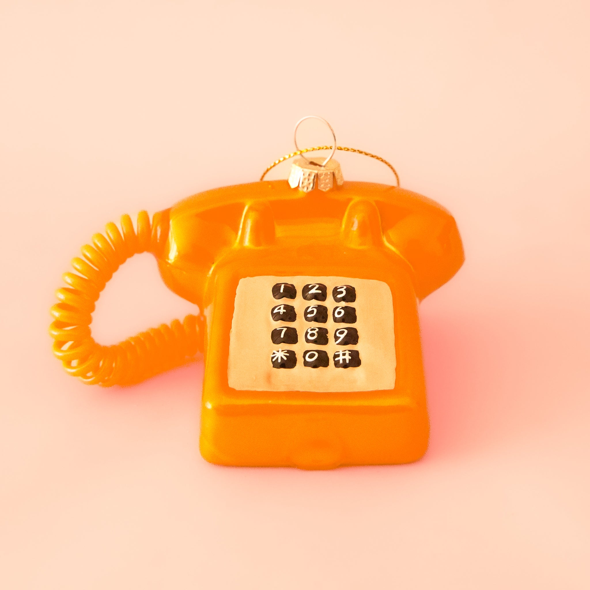 A touch tone phone ornament in a shiny orange color on a bright orange background. 