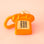 A touch tone phone ornament in a shiny orange color on a bright orange background. 