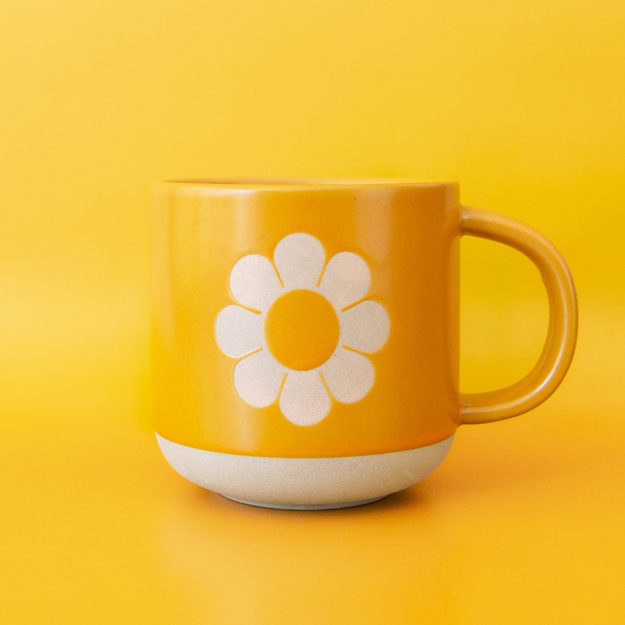 A yellow ceramic mug with a flower shape in the center. 