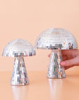 On a peach background is two different sized disco mushrooms with mirrored square pieces all over. 