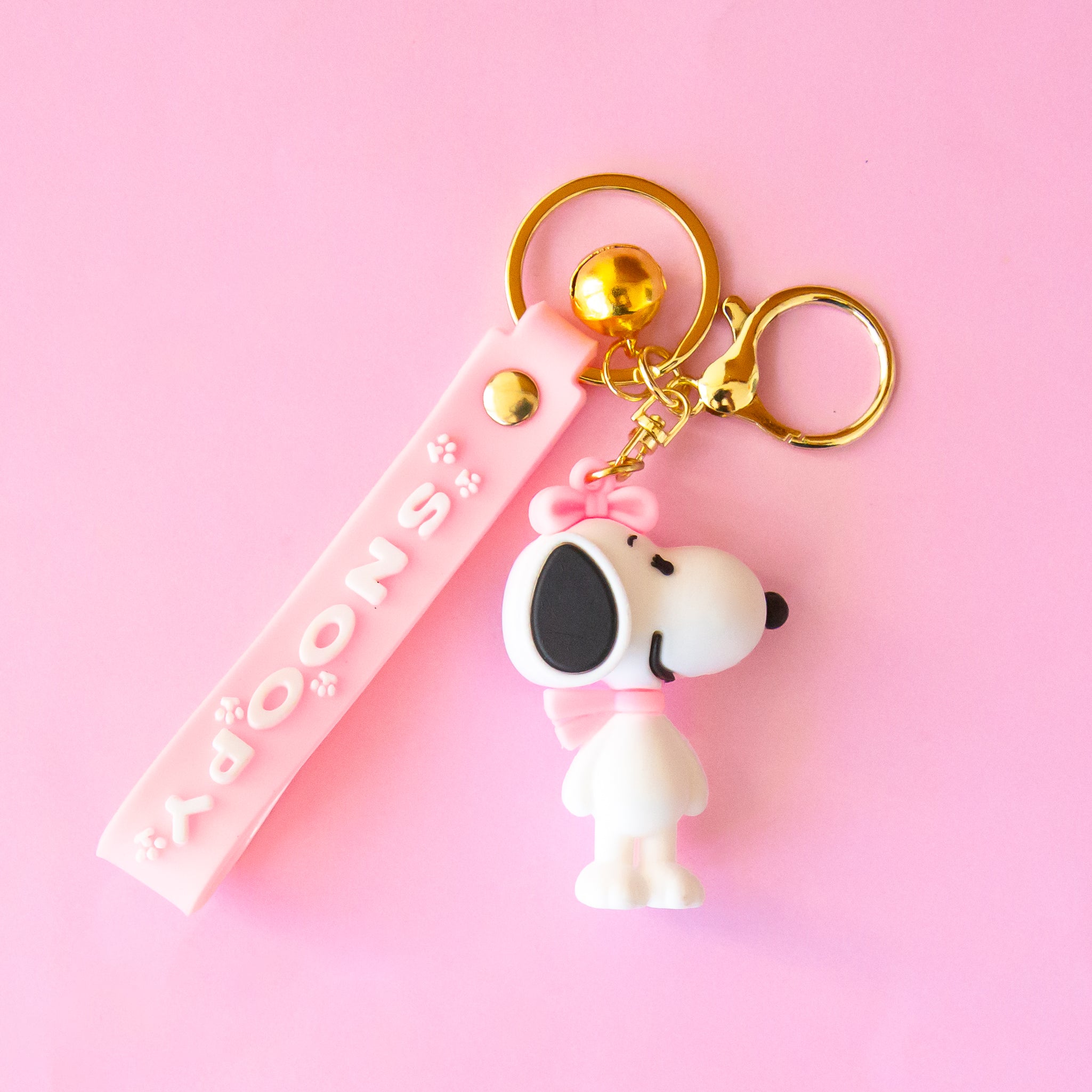 A snoopy shaped keychain with a pink lanyard that reads, "Snoopy". 