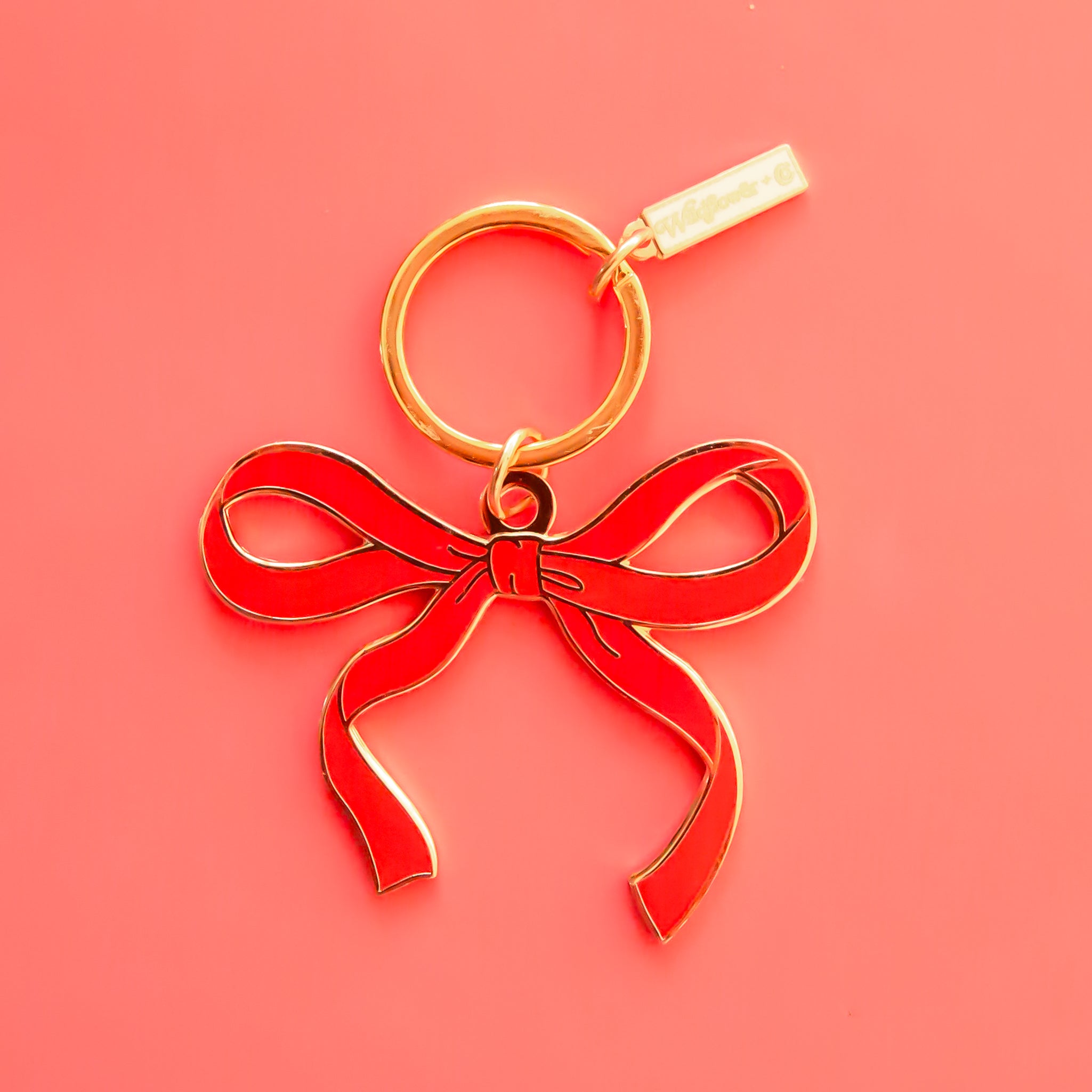 red bow shaped aenamel keychain on gold ring lays on an orange piece of paper.