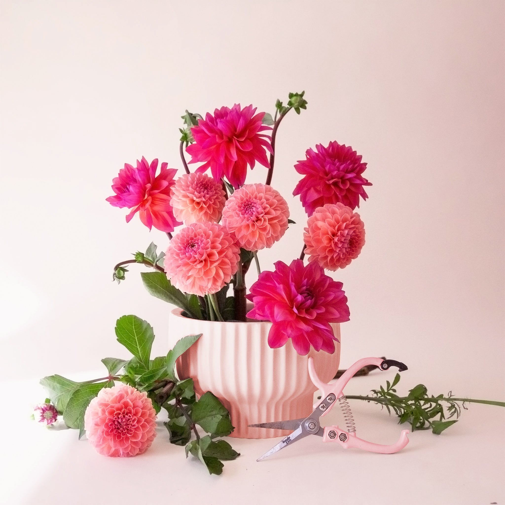 On a tan background is a pink ceramic ribbed pedestal pot filled with cut flowers not included with purchase. 