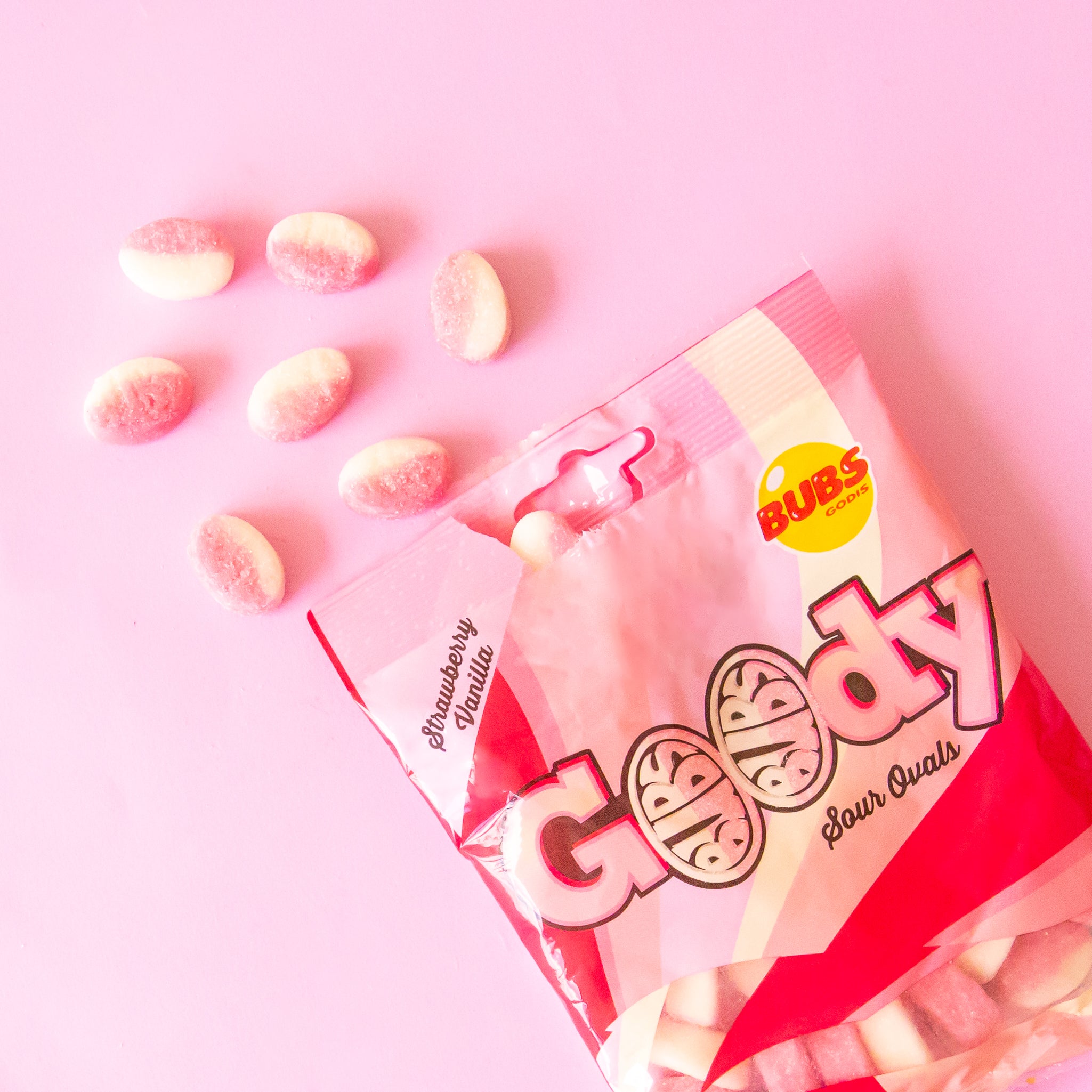 a bag of pink and white striped candies spills onto a pink ground.  Several candies are falling out of a bag that reads &quot;Goody sour Ovals&quot; they are marked as &quot;strawberry vanilla&quot; flavor.