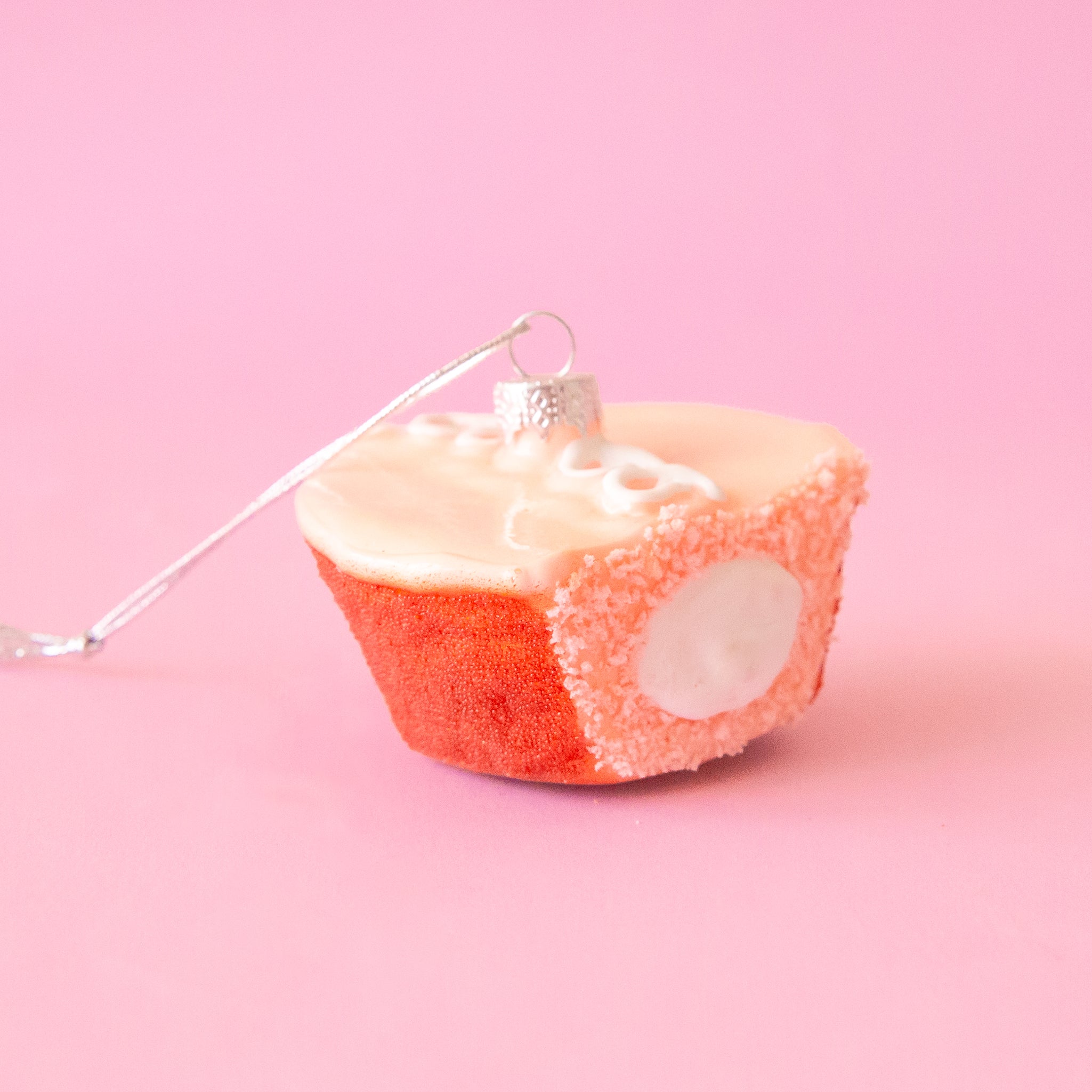 ornament of a pink cupcake with white icing and a bite taken out of it.  There is a white creme filling exposed on the size of the pink cake.
