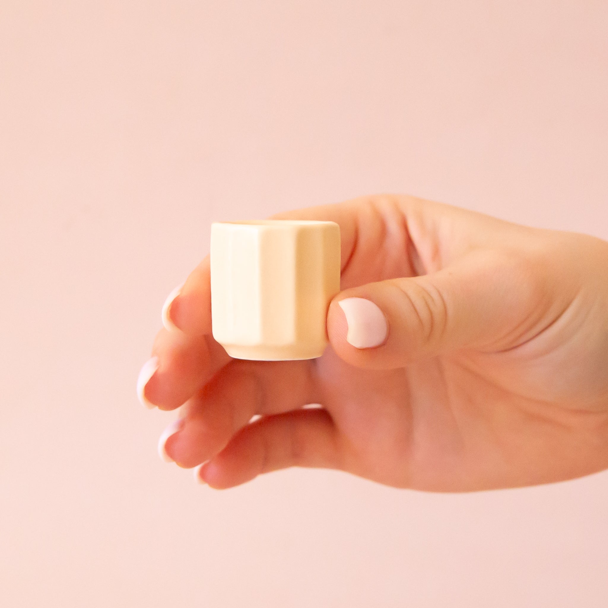 An itty bitty pot about the size of thimble that is a soft beige color sits in the middle of a page.  The background is all a soft white color.