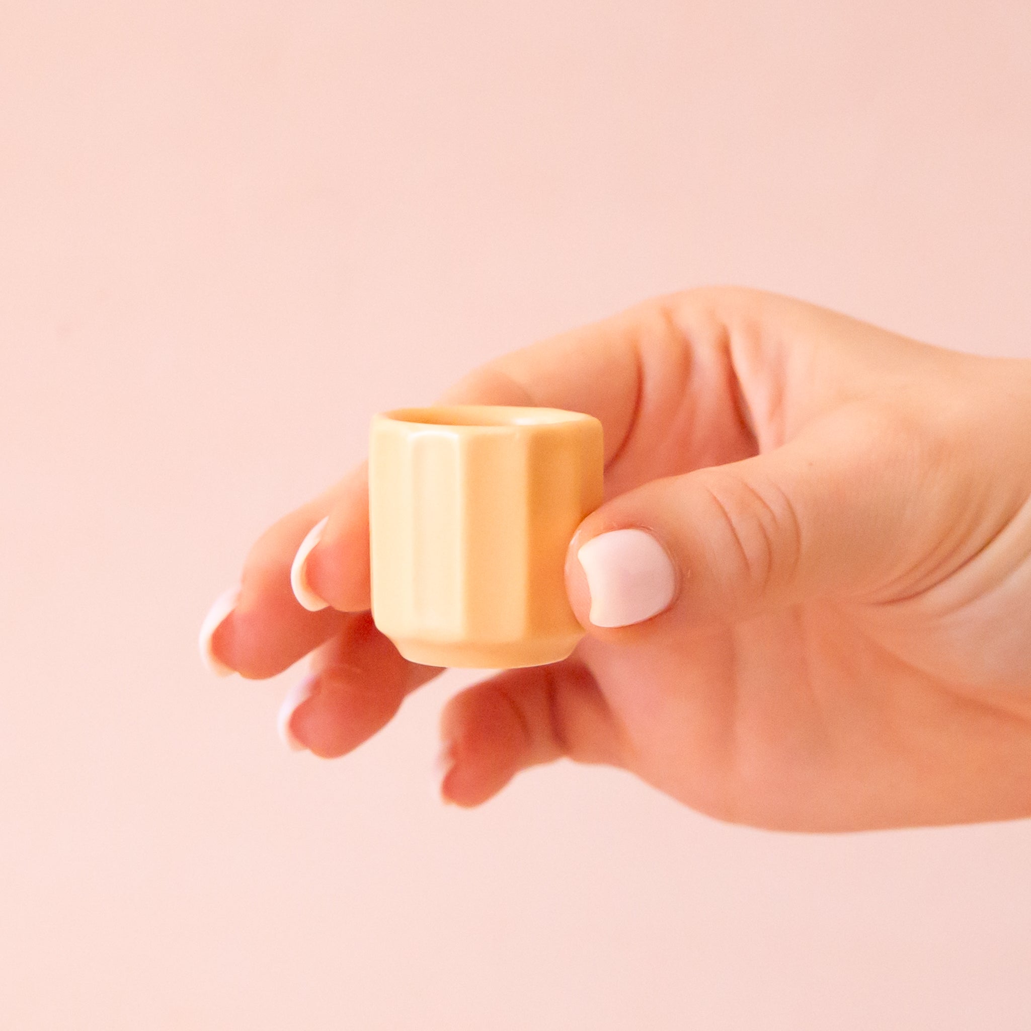 An itty bitty pot about the size of thimble that is a soft peach color sits in the middle of page.  The tiny pot has little ridges all around it.  The background is all  a soft white color.