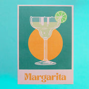 margarita shaped glass with lime wheel on rim over a green background with orange circle. text reads margarita.