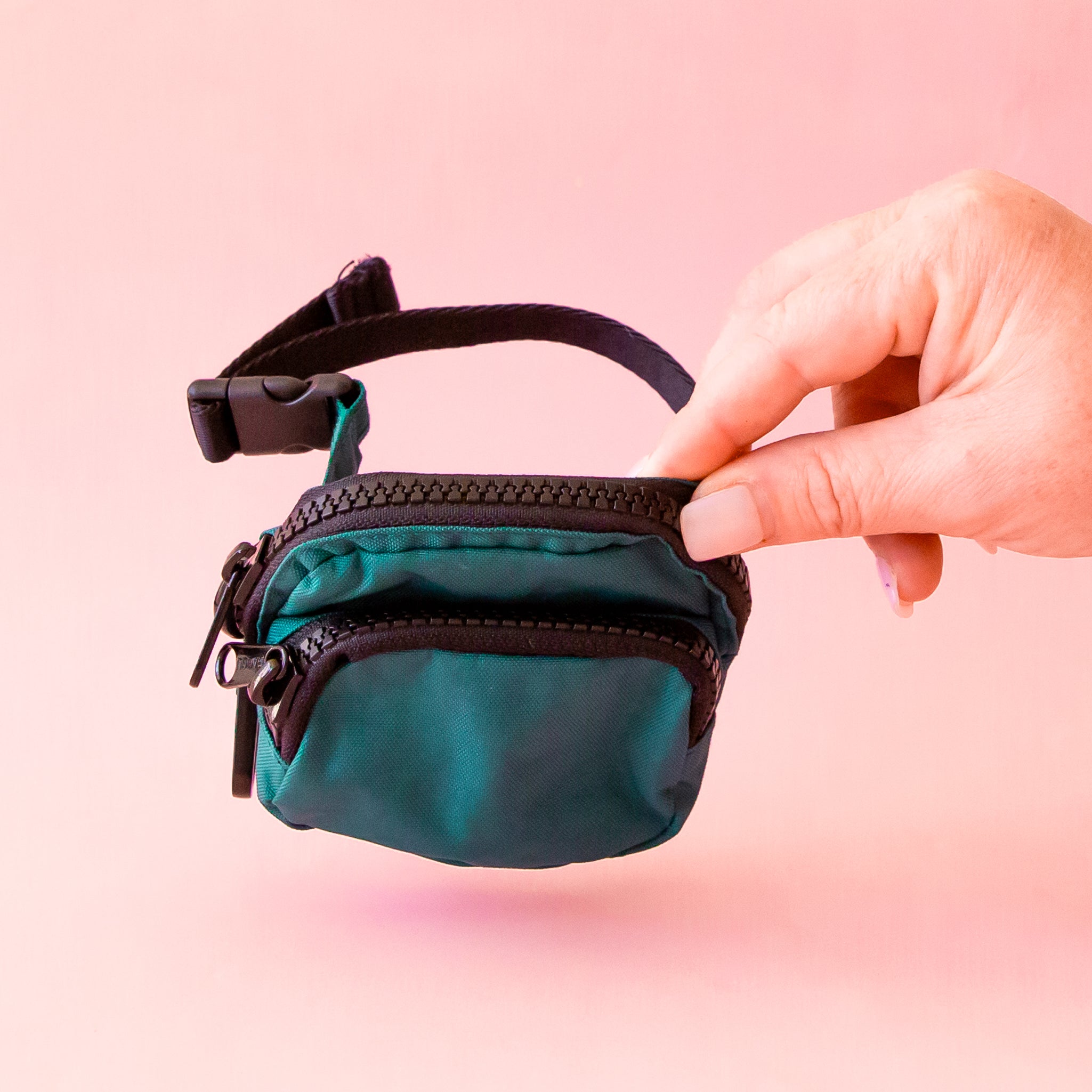 A cypress green colored fanny pack bag charm with black zippers and details. 