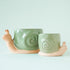 Two ceramic planters in the shape of a snail with smiling faces and a swirly green "shell". 