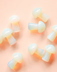 On a pink background is a handful of mini opal mushroom shaped crystals. 