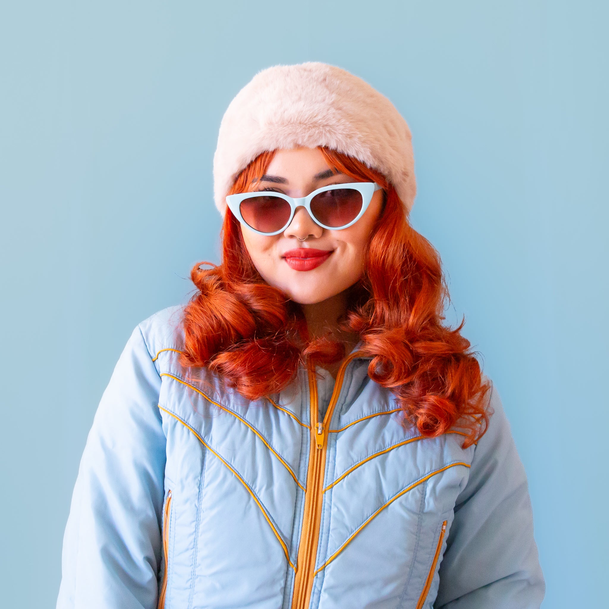 A model wearing an oatmeal colored faux fur headband against a light pink background. 