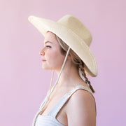 A bone colored straw cowboy style hat with a rope neck tie detail.