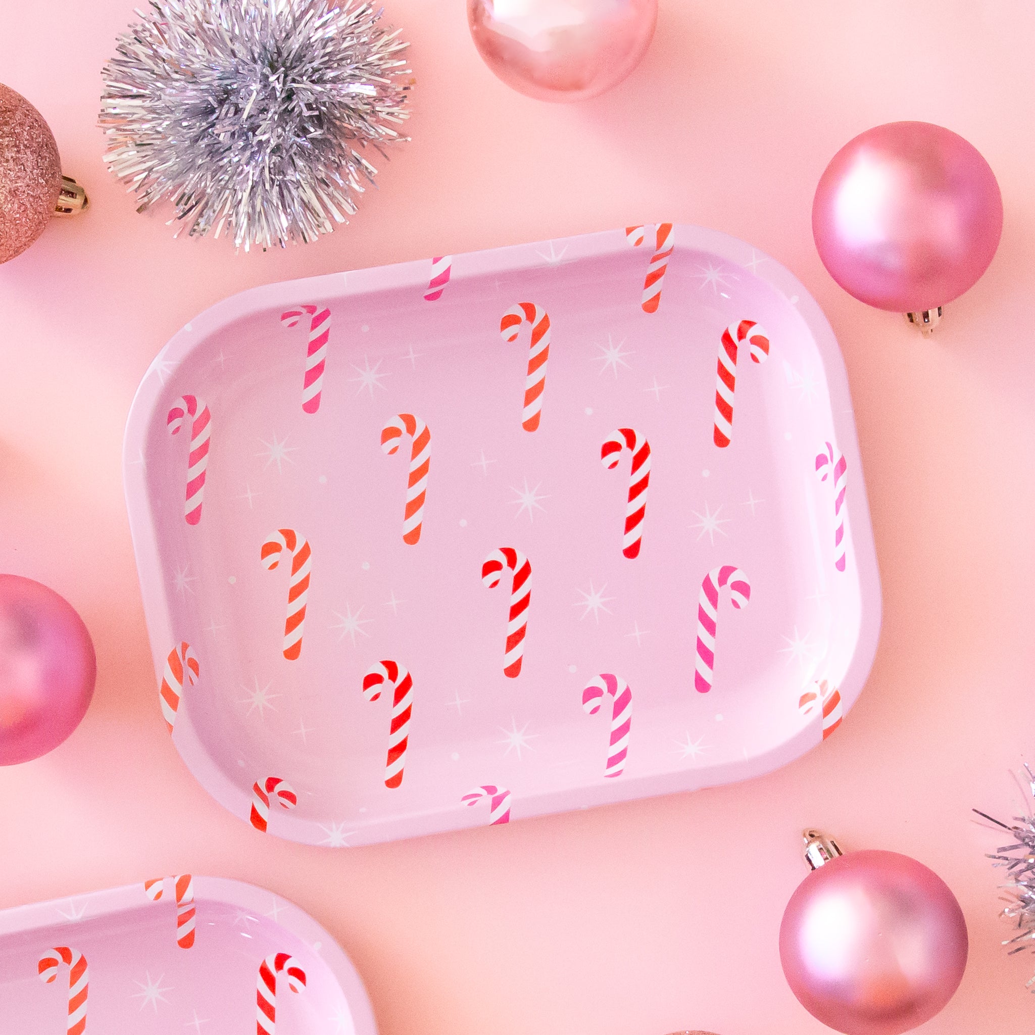 The tray has pink, orange and red candy canes on it with white sparkle detail.  The background of the image is a soft pink color