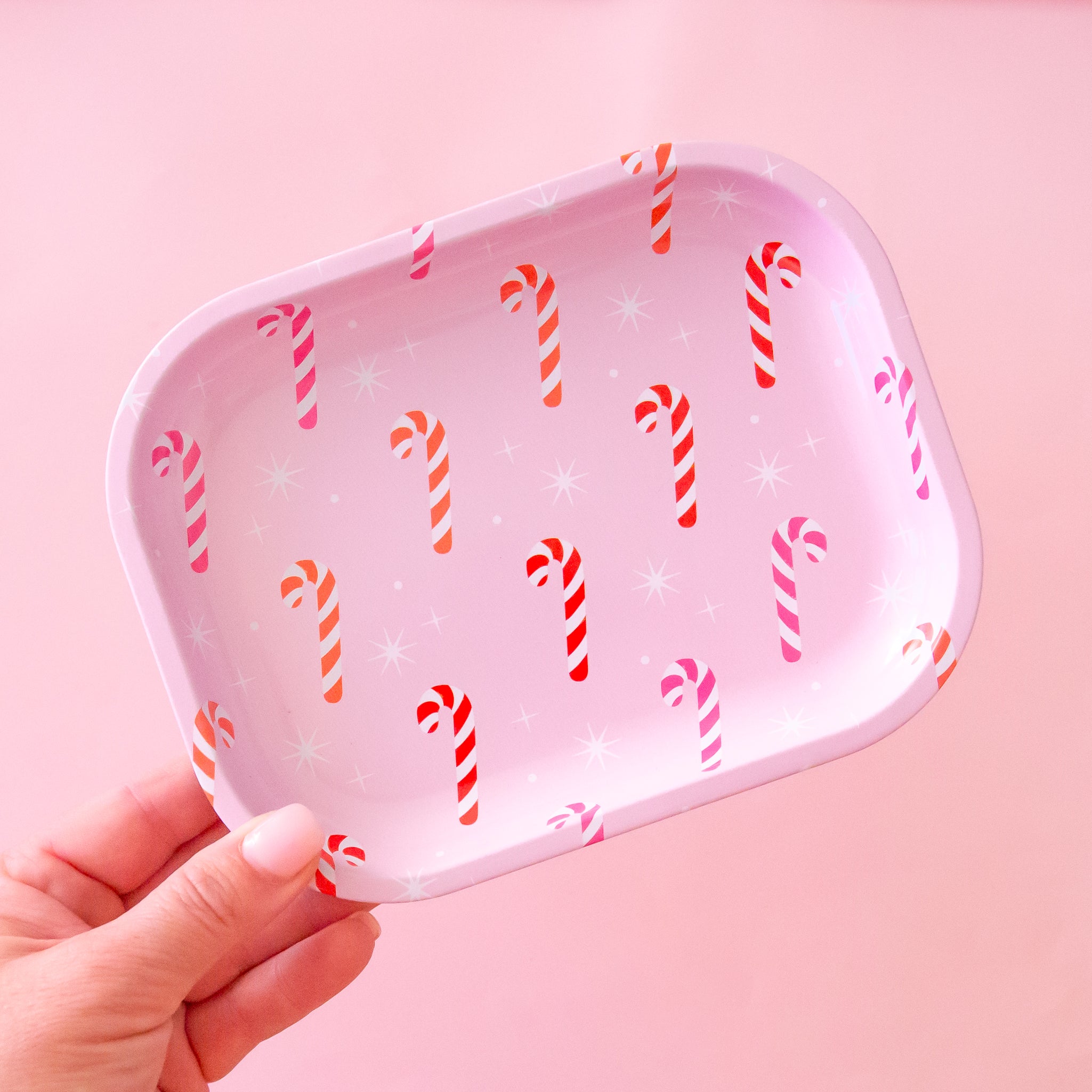 The tray has pink, orange and red candy canes on it with white sparkle detail.  The background of the image is a soft pink color