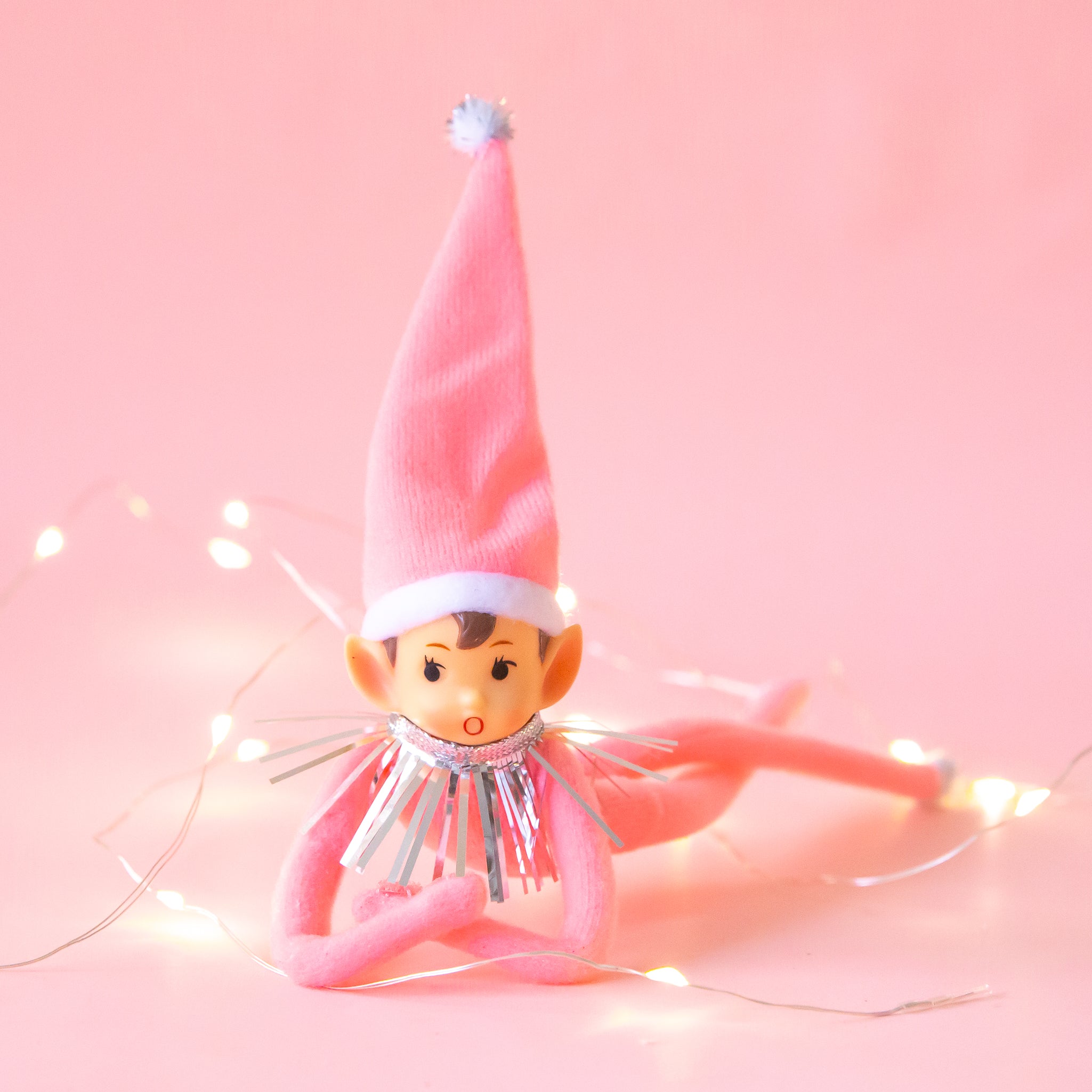 An adorable pink elf wearing a pink tall hat with silver tinsel around its neck.