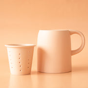 On a neutral background is a ceramic mug with an infuser cup to insert inside the rim of the mug.