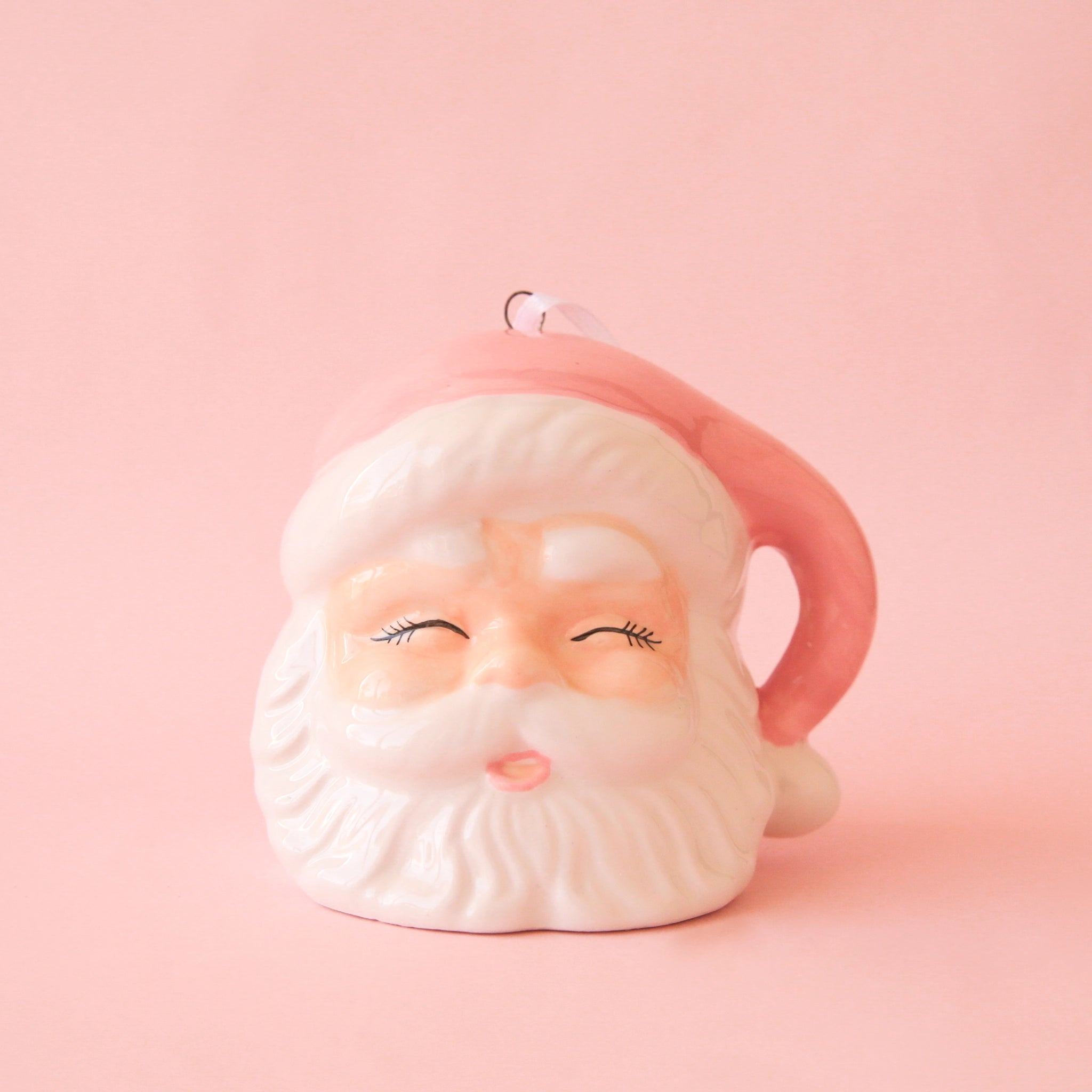 On a pink background is a white and pink Santa head ornament with eyes closed and a pink hat. 