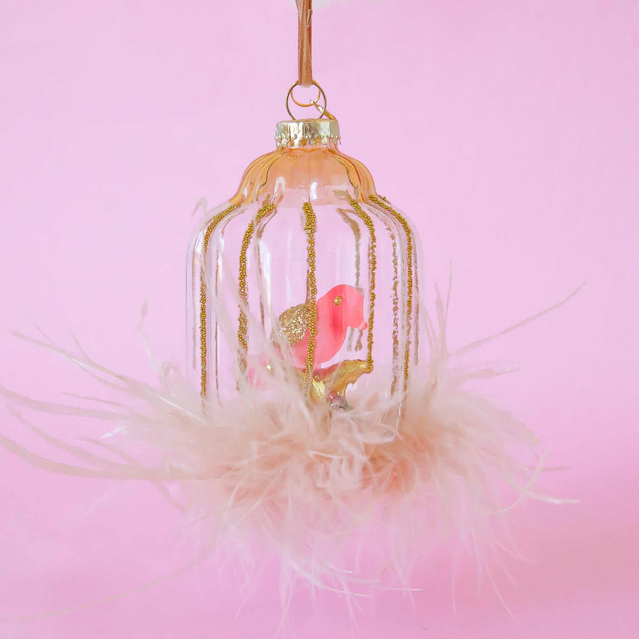 A glass bird cage ornament with a pink bird shape inside and pink feather details. 