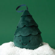 On a green background is a dark green Christmas tree stuffed toy with a smiling face and a loop at the top for an option to hang on a tree or mantle for festive fun.