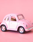 On a pink background is a pink and white two toned toy in the shape of a volkswagen beetle. 
