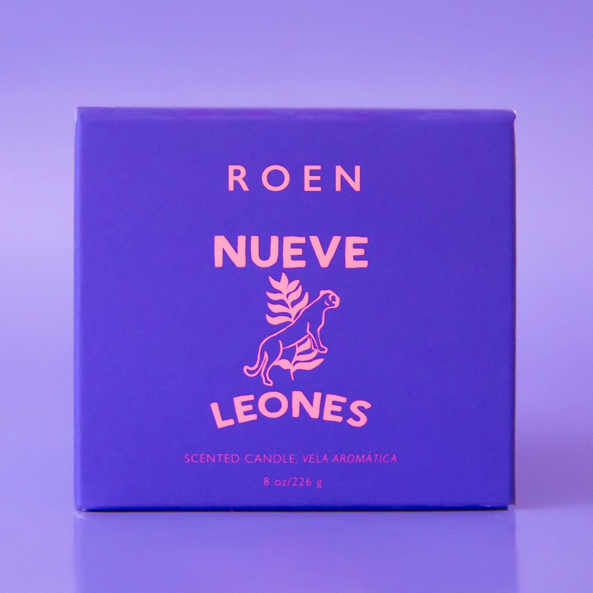 A purple glass candle with a white label with, &quot;Nueve Leones&quot;.