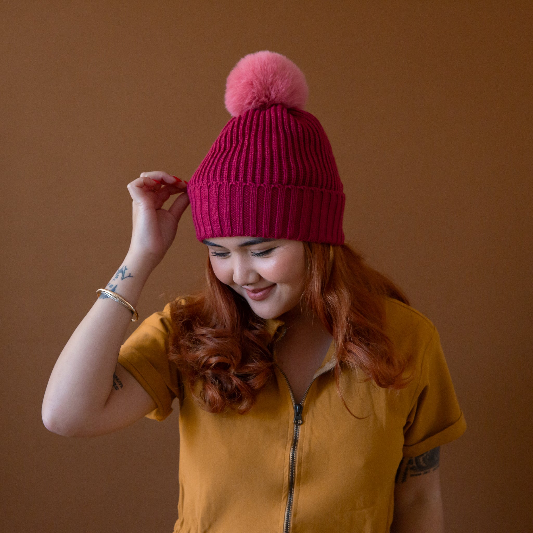 A model wearing a dark pink beanie with a lighter pink pom at the top. 