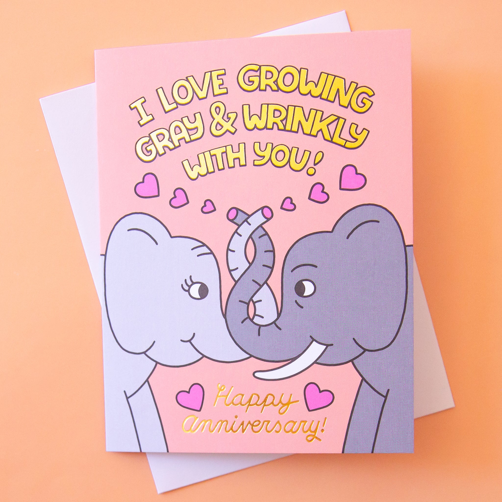 On a orange background is a card with a graphic of elephants intertwining trunks and text above and below that reads, &quot;I Love Growing Gray &amp; Wrinkly With You! Happy Anniversary&quot;. 