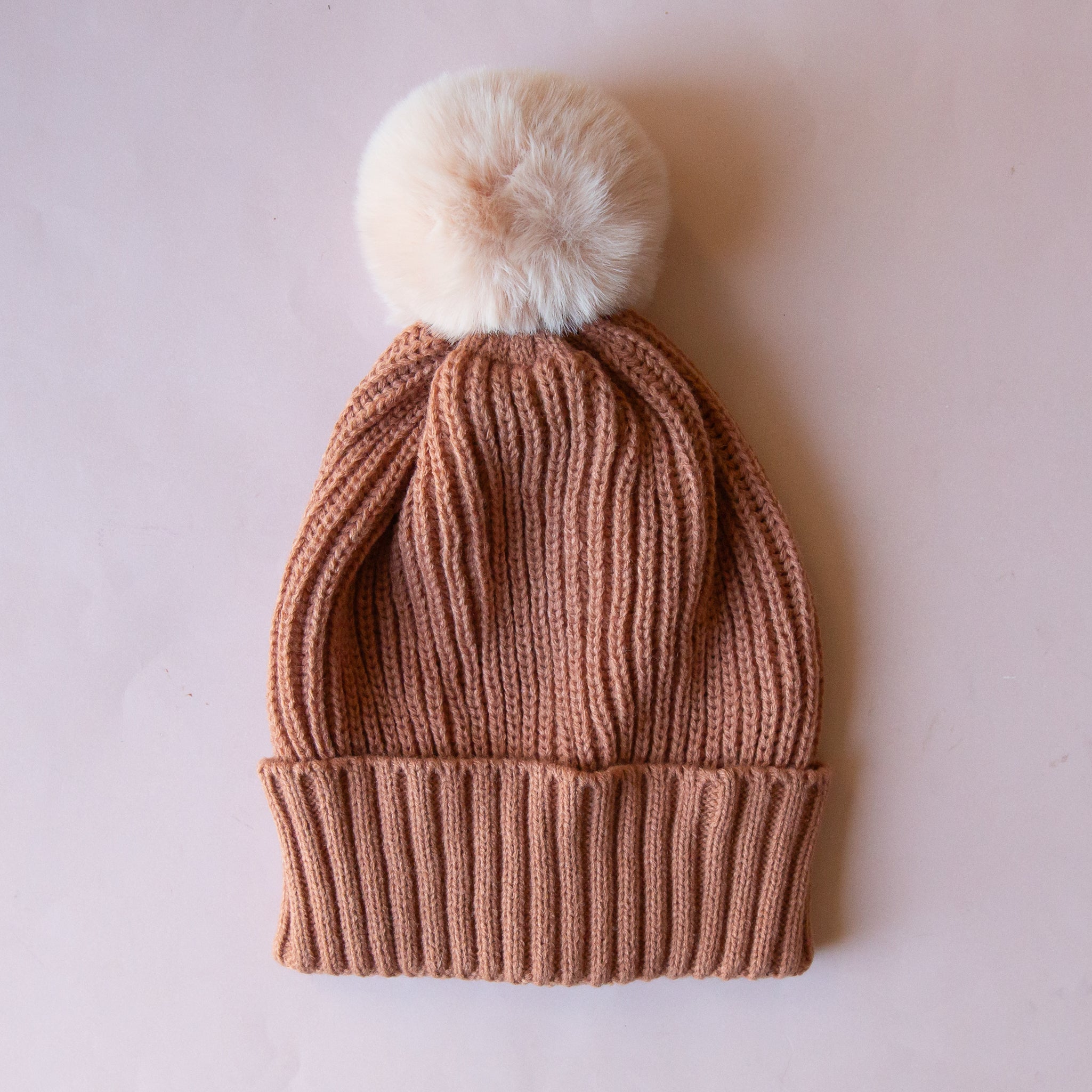 A light brown beanie with a neutral pom at the top. 