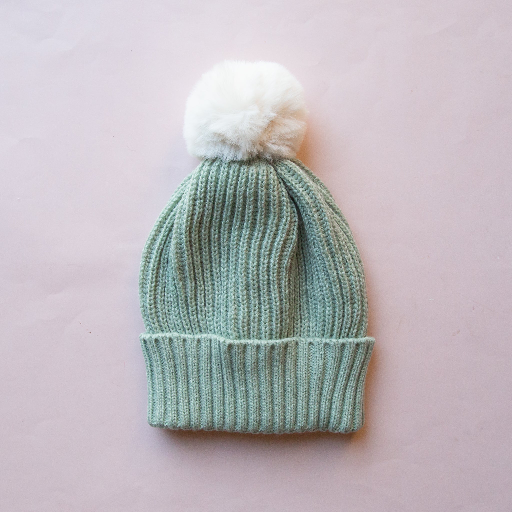 A mint green knit beanie on a model with a white pom at the top. 