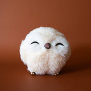 On a brown background is a white round owl ornament with faux fur and closed eyes. 