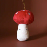 On a brown background is a red and ivory mushroom shaped ornament with a velvet top and corduroy base as well as a closed eye expression. 