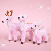 On a pink sparkle background is three fur reindeer ornaments.