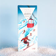 On a light blue background is a rectangle chocolate bar with packaging that features a mountain and skiers in red outfits along with text at the top that reads, "Compartes Hot Cocoa & Marshmallow Dark Chocolate".