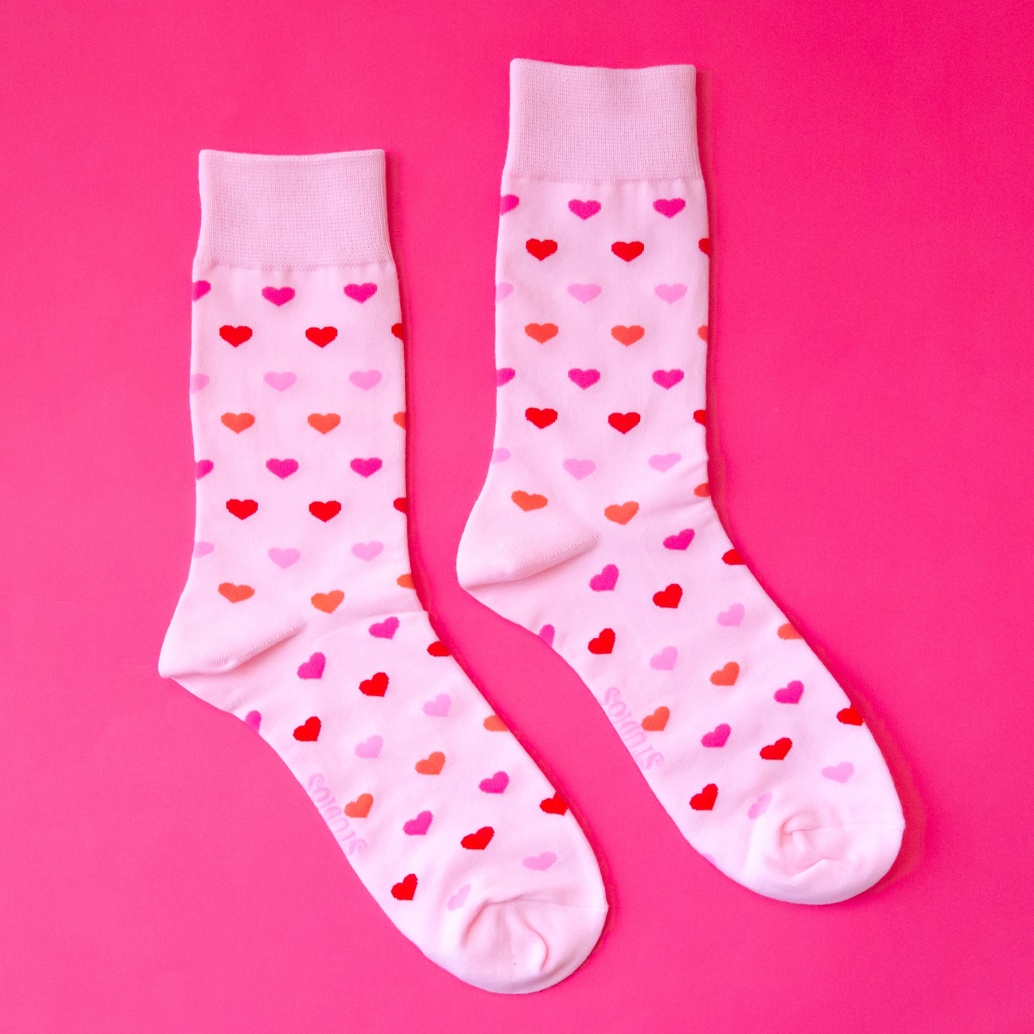 A pair of crew socks with a heart print that is in different shades of pink. 