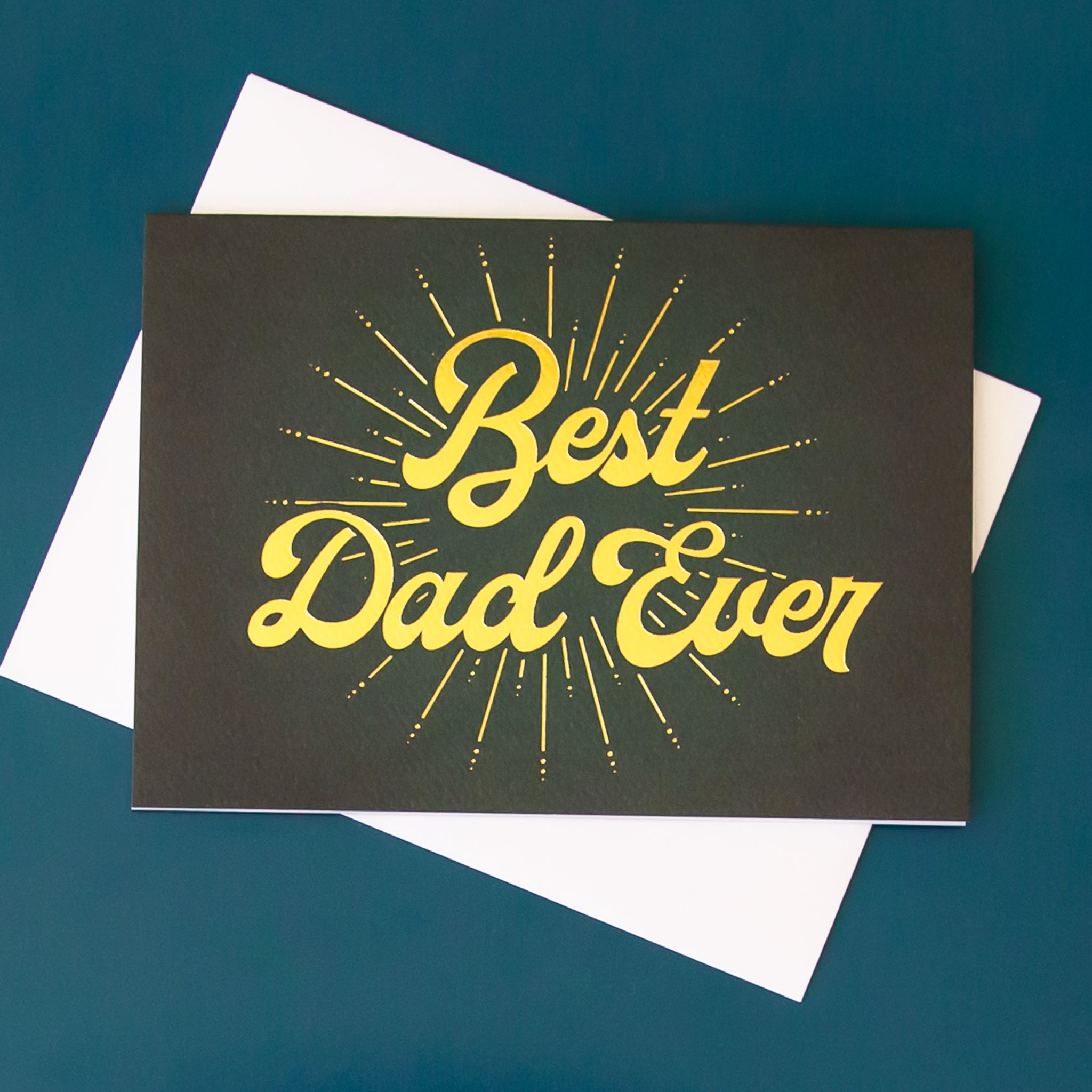 On a blue background is a dark greenish black Father's Day card with gold text across the front that reads, "Best Dad Ever".