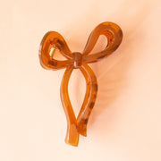 On a peachy background is a brown bow shaped claw clip. 
