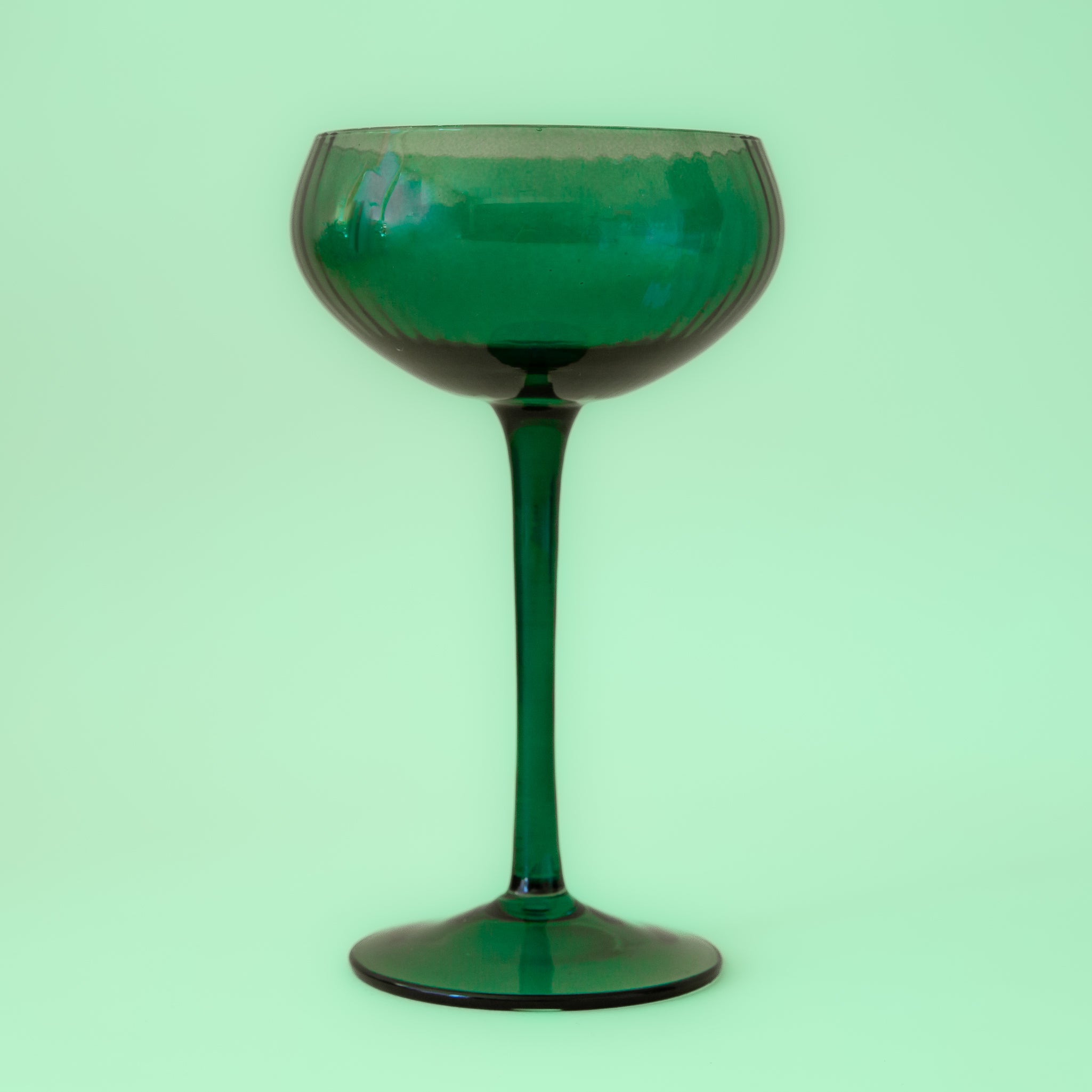 On a green background is a green glass coup glass with a subtle ribbed texture. 