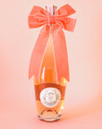 On a peachy background is a bottle of wine with a velvet peach colored bow on.